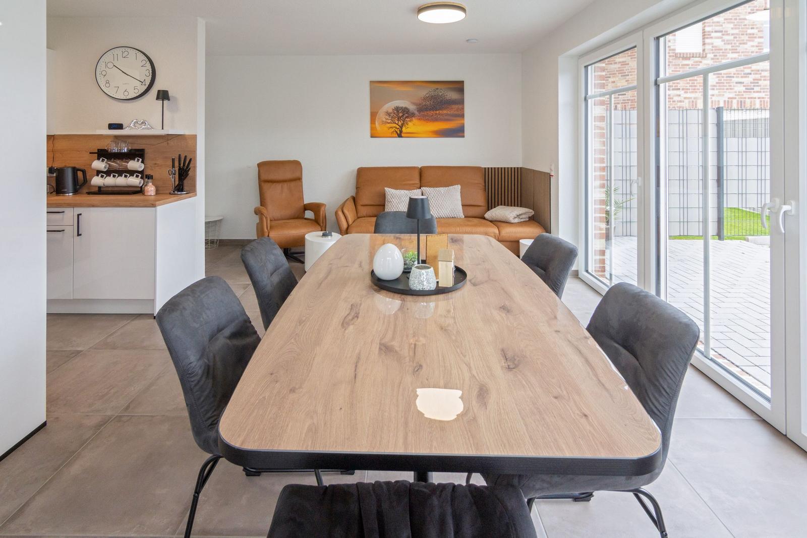 Essbereich mit Holztisch und Stühlen, Wohnbereich mit Sofa und Sessel, Terrasse über Glastür