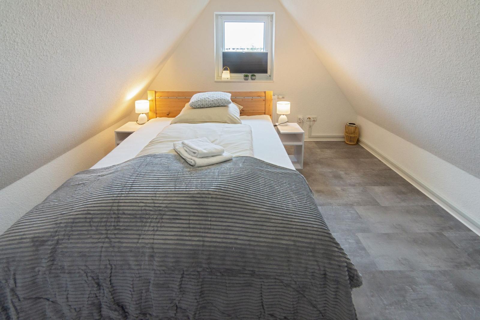 Schlafzimmer mit Dachschräge, Bett, Nachttischen und Fenster.