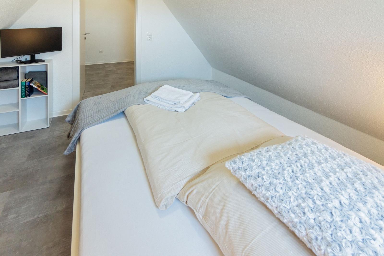 Schlafzimmer mit Dachschrägen, Bett mit Bettwäsche, Fernseher und Schrank.