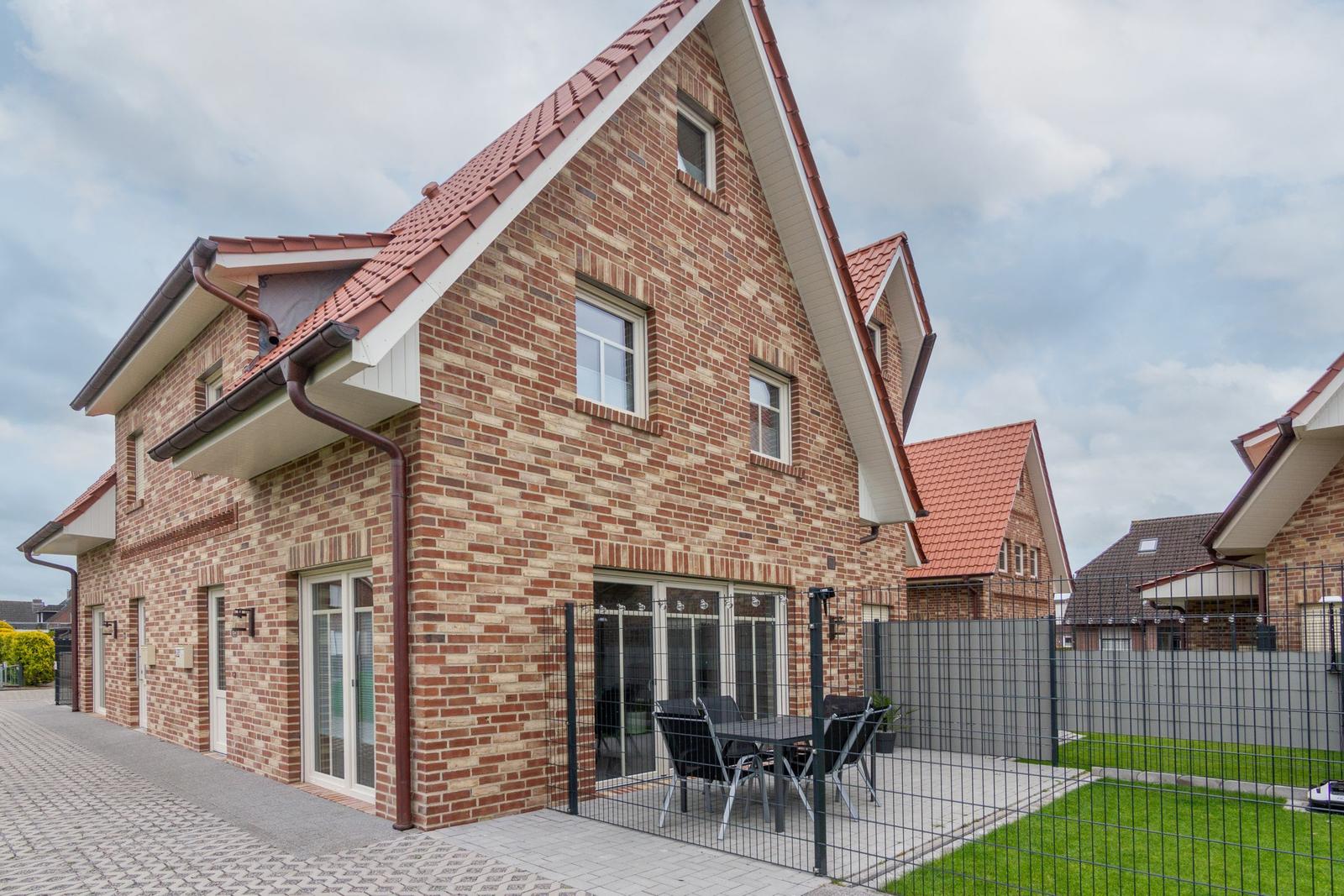 Zweistöckiges Haus mit Terrasse und Garten. Roter Ziegeldach, Fenster und Türen.
