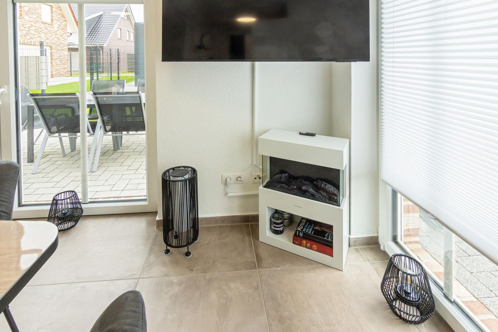 Wohnzimmer mit Fernseher, elektrischem Kamin und Blick auf die Terrasse.