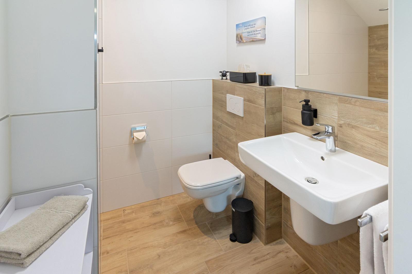 Badezimmer mit Toilette, Waschbecken und Dusche. Holzoptik an Wänden und Boden.