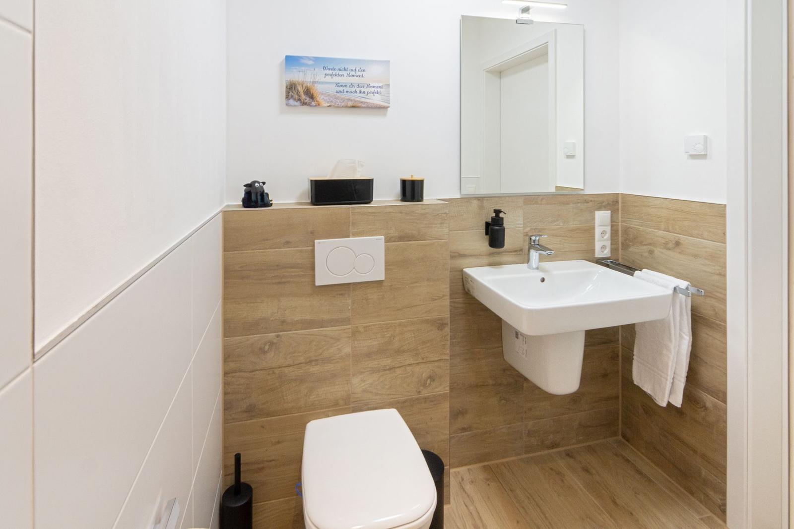 Badezimmer mit Toilette, Waschbecken und Spiegel an Holzwand