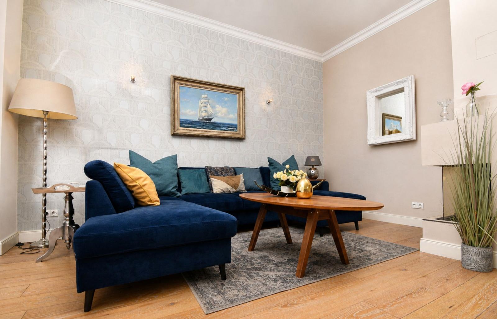 Ein Wohnzimmer mit blauem Sofa, Holztisch und Wandbild mit Segelschiff.