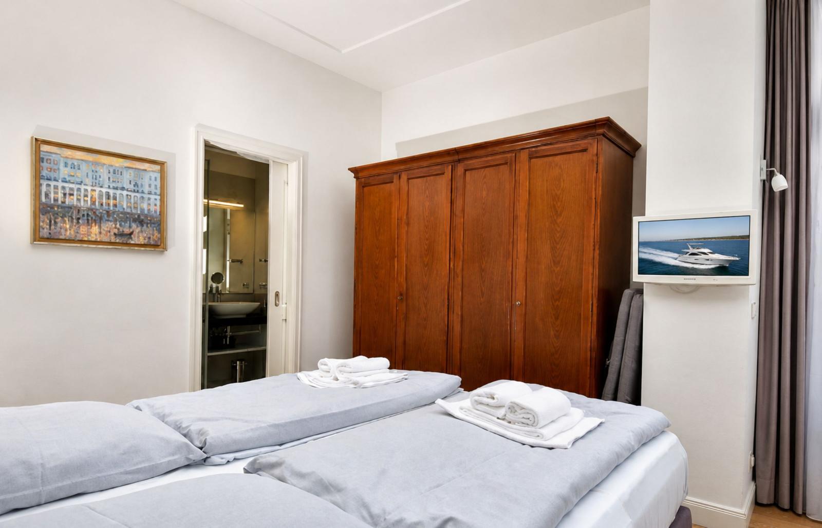 Zimmer mit Doppelbett, Holzschrank und TV. Badezimmer ist angebaut.