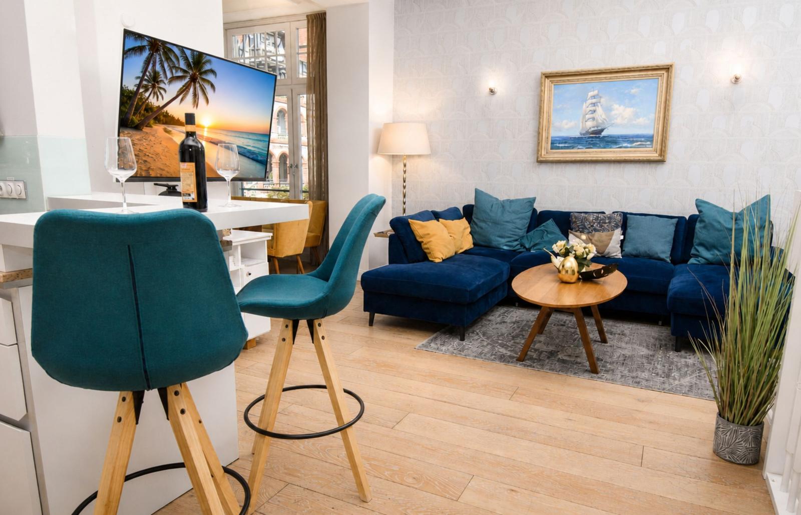 Wohnbereich mit blauem Sofa, Holztisch und TV. Helle Holzböden und Wanddekoration.
