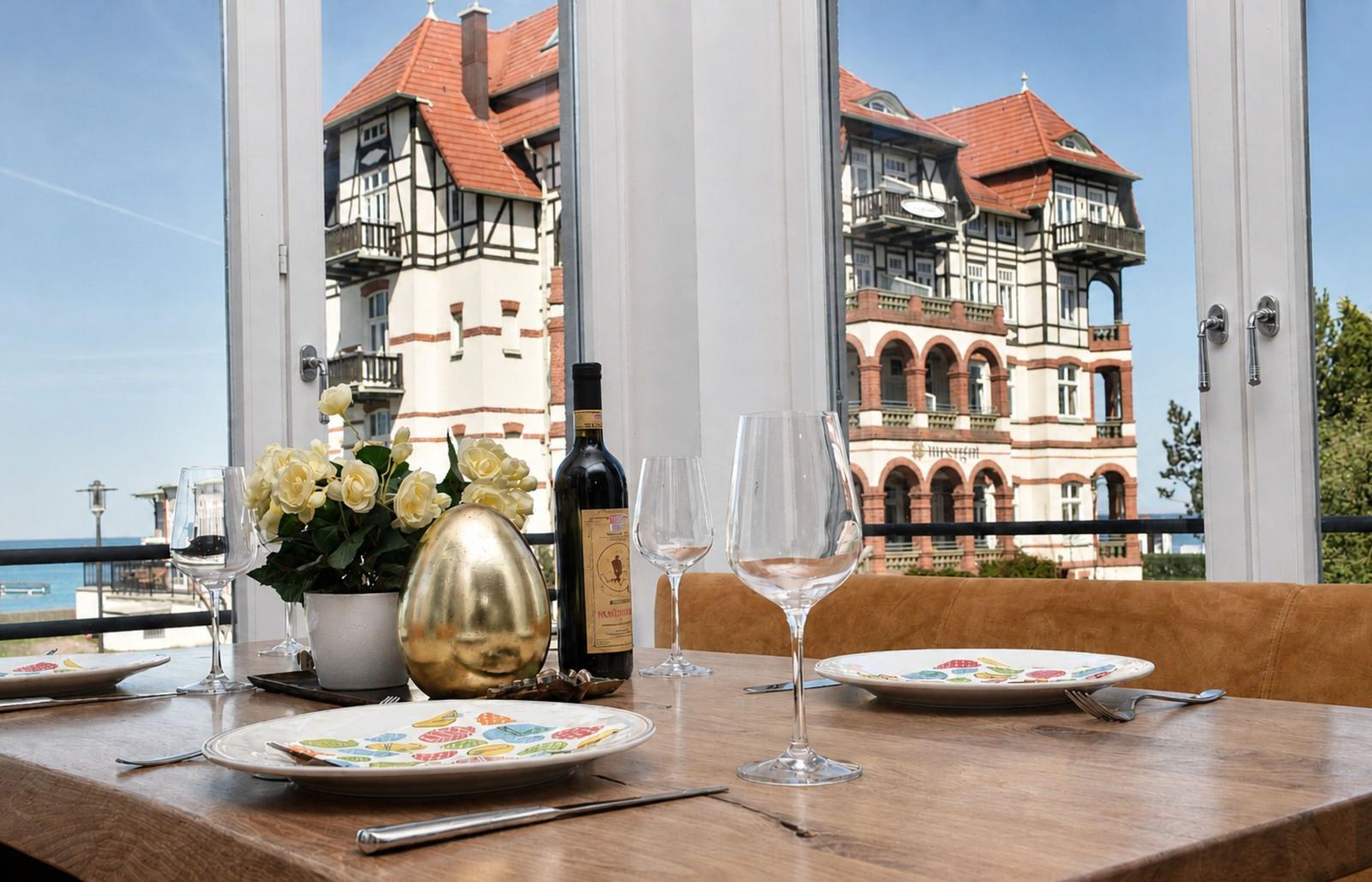 Esstisch mit Wein und Blick auf historisches Gebäude und Meer.