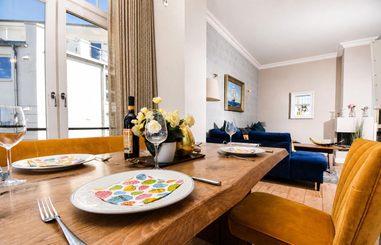 Essbereich mit Holztisch, gelben Stühlen und blauem Sofa im Hintergrund.