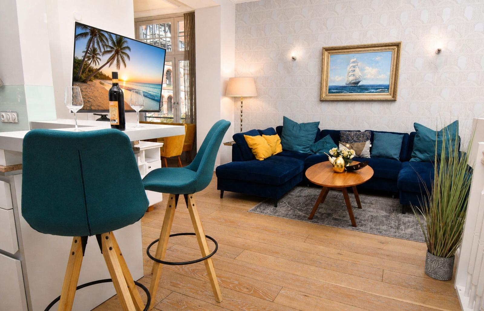 Wohnbereich mit blauem Sofa, Holztisch und Fernseher an der Wand.