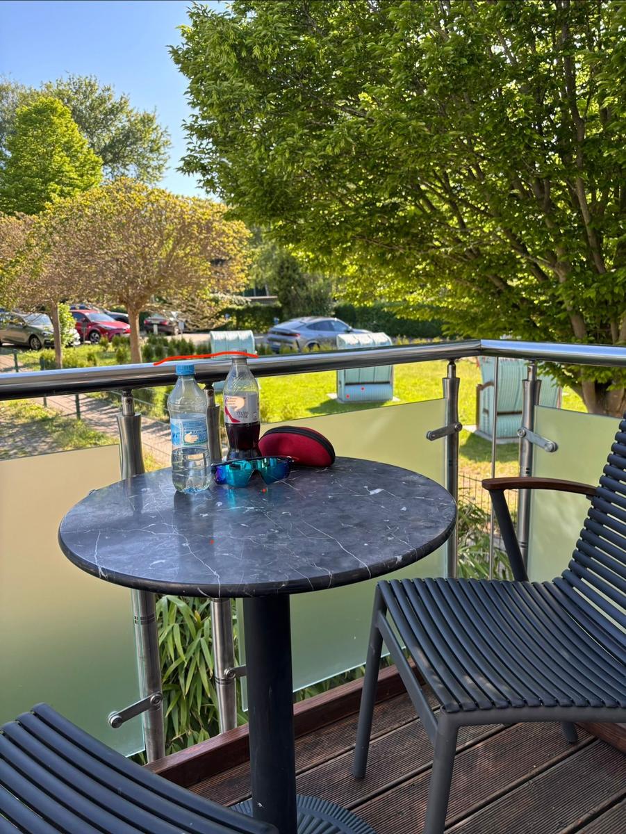 Terrasse mit Tisch, Stühlen und Blick auf grüne Bäume und Parkplatz.