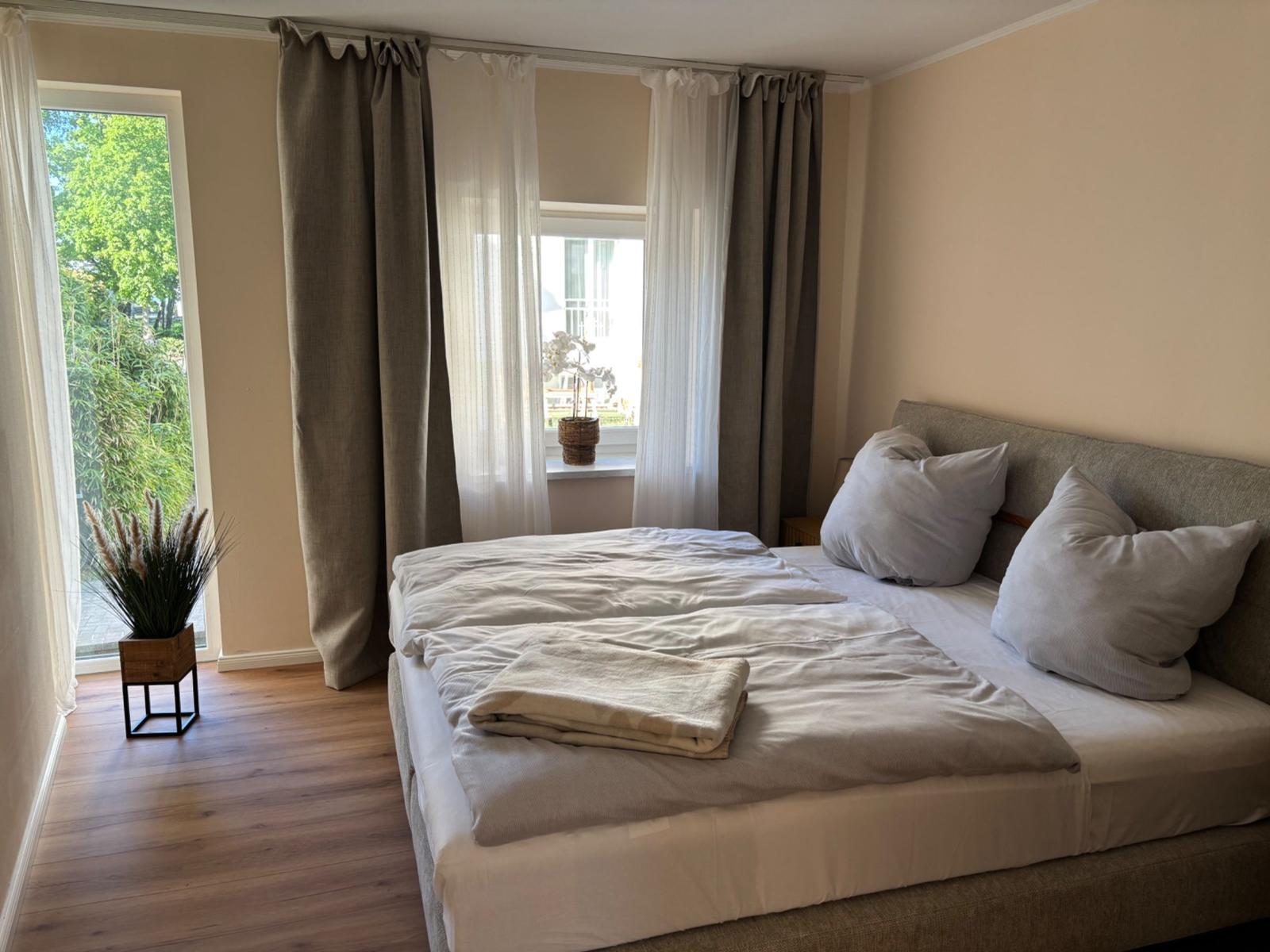 Ein Schlafzimmer mit Bett, Vorhängen und Fensterblick auf Grün.