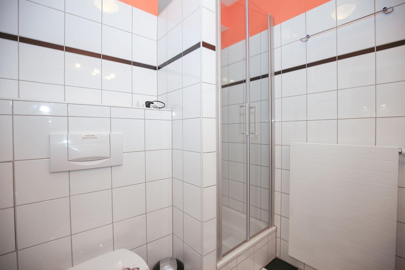 Badezimmer mit Dusche, Toilette und Heizkörper an der Wand.