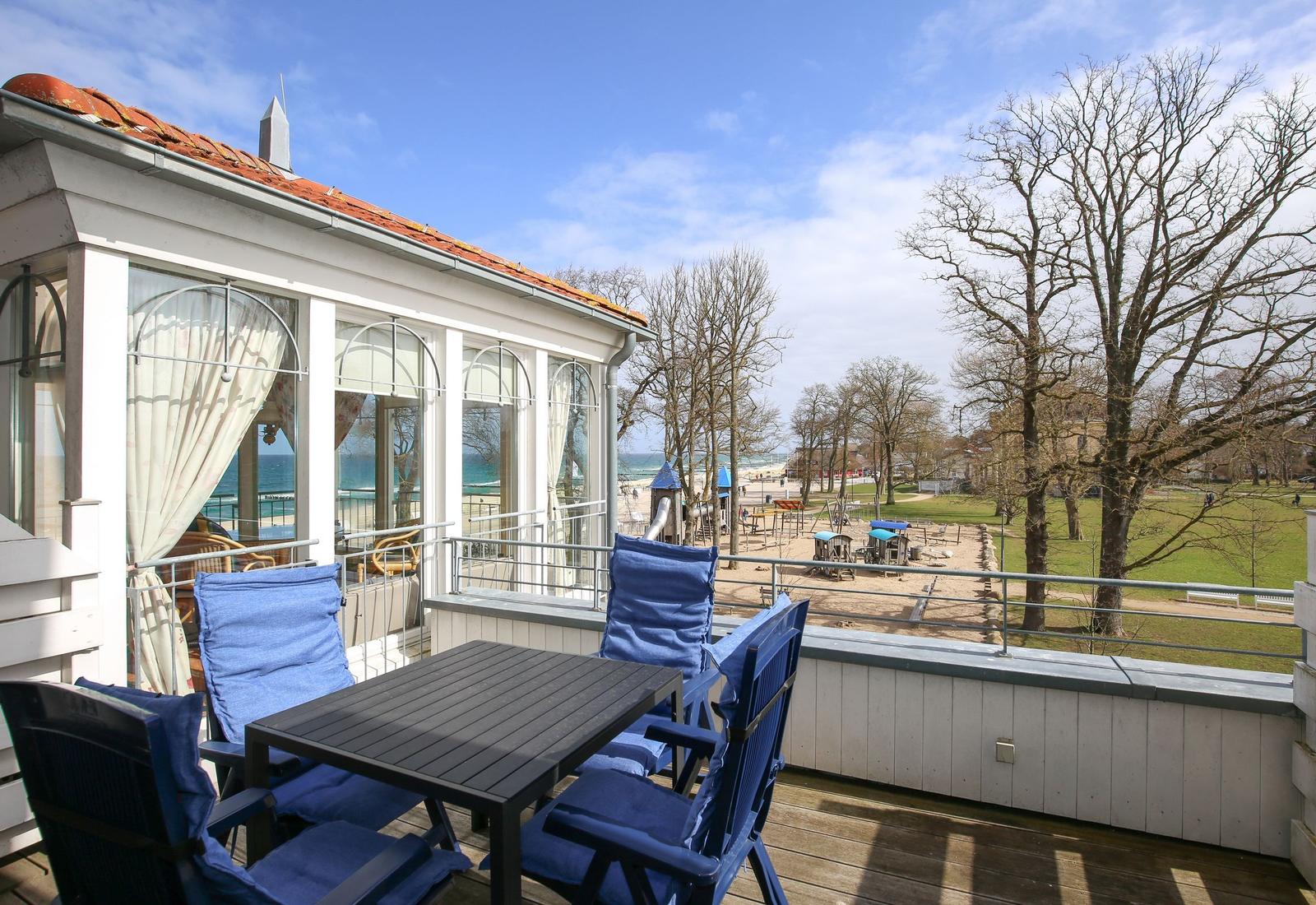 Terrasse mit Tisch und Stühlen, Blick auf Spielplatz und Strand.