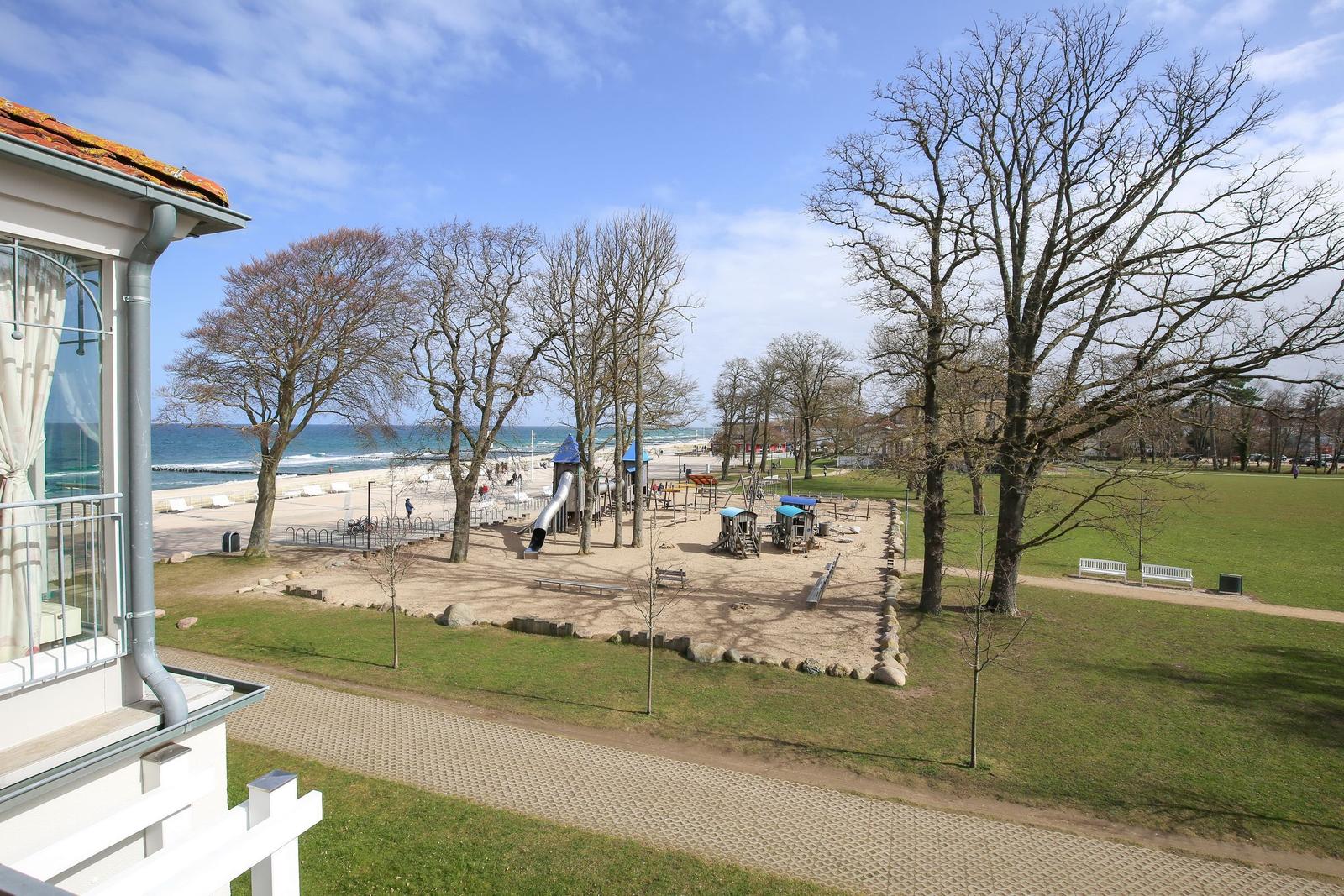 Von der Terrasse aus Blick auf Spielplatz, Strand und Meer unter blauem Himmel.