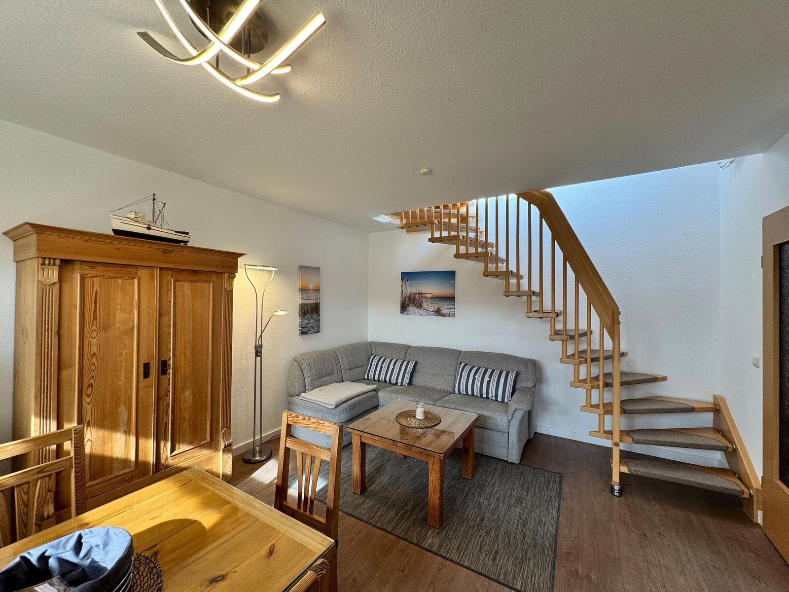Wohnzimmer mit Sofa, Tisch und Holztreppe. Holzschrank und Wandbilder sichtbar.