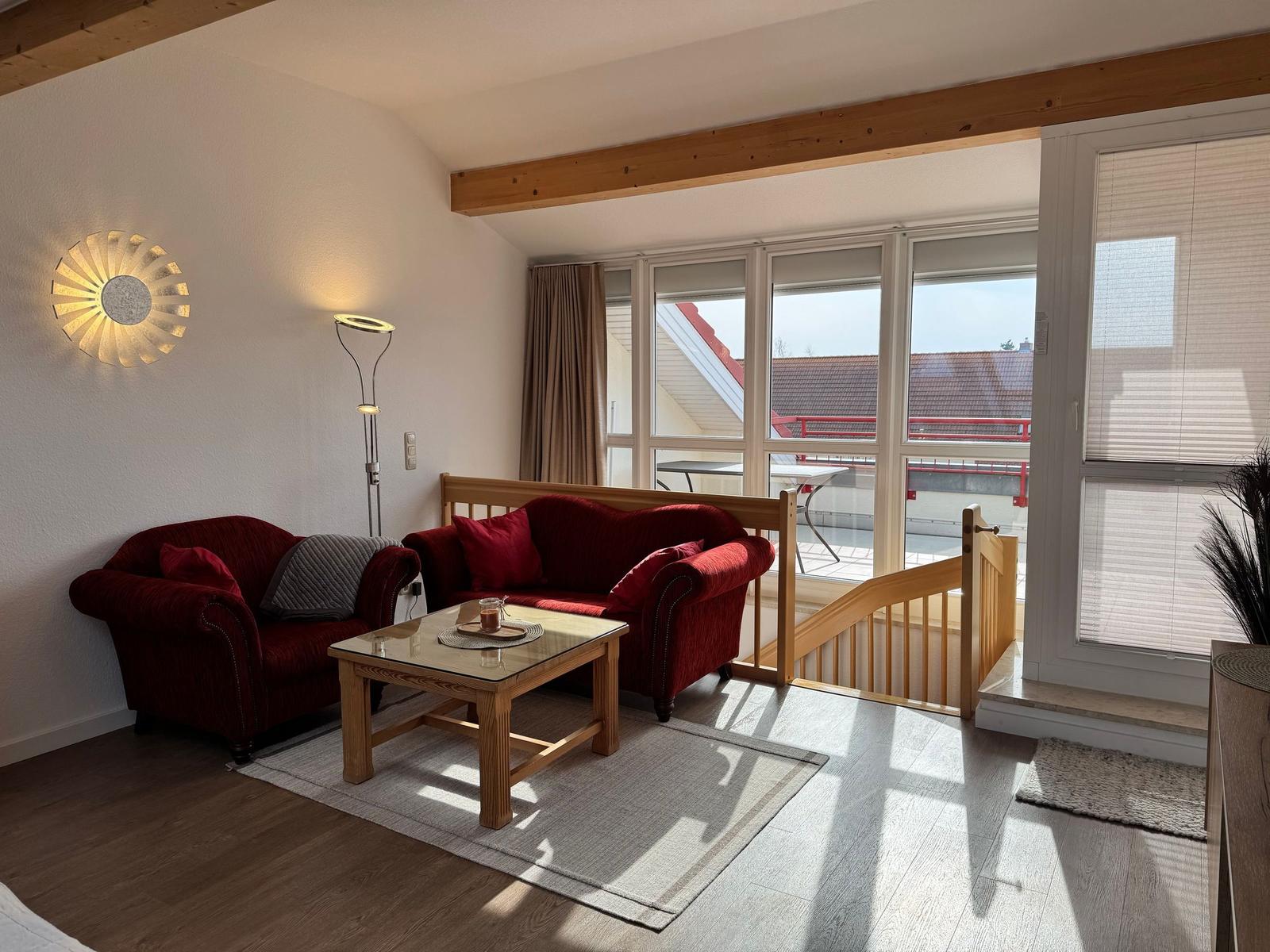 Ein Wohnzimmer mit rotem Sofa, Holztisch und Balkonzugang.