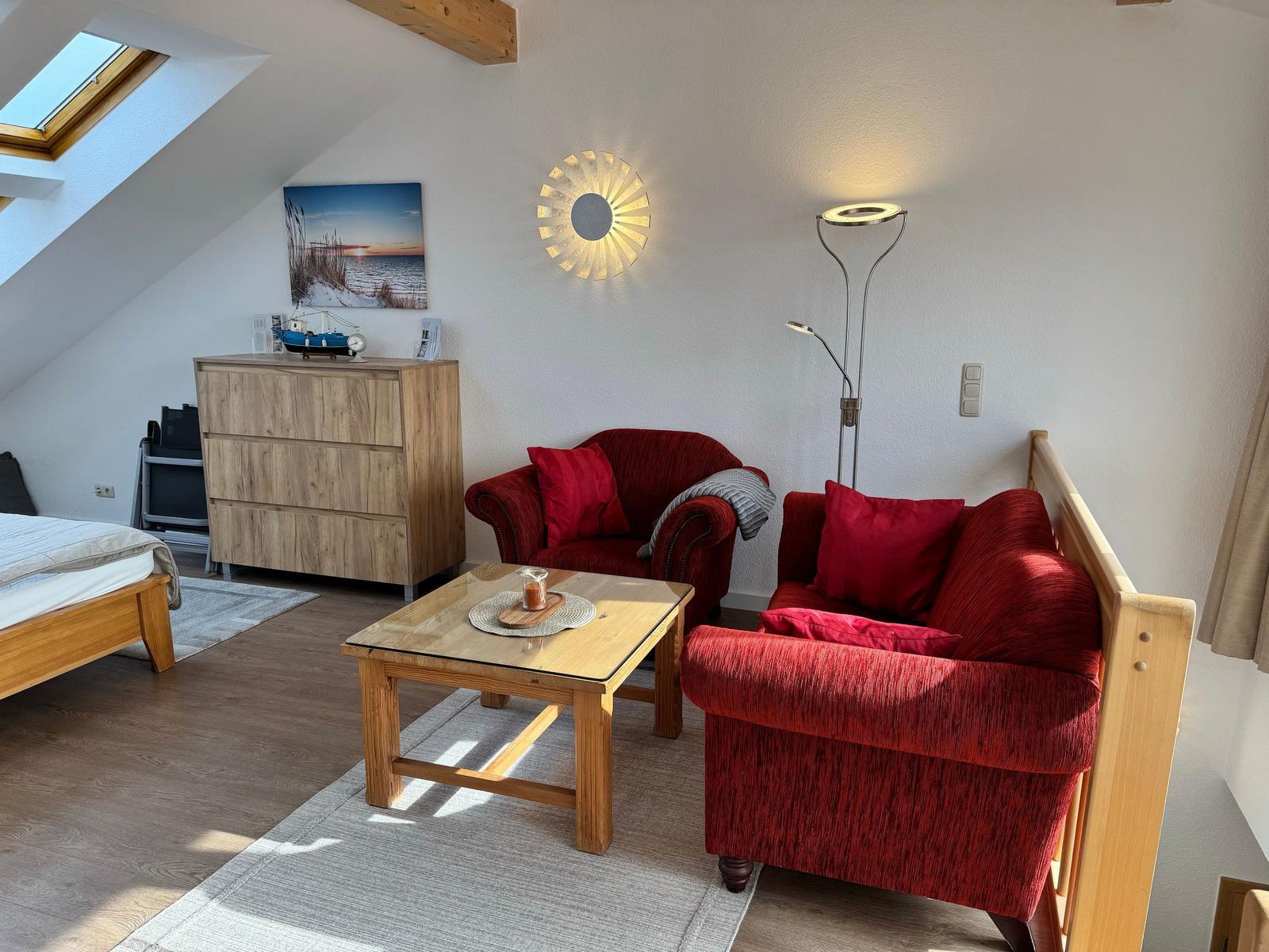 Ein Schlafzimmer mit rotem Sofa, Holzmöbeln und Dachfenster.