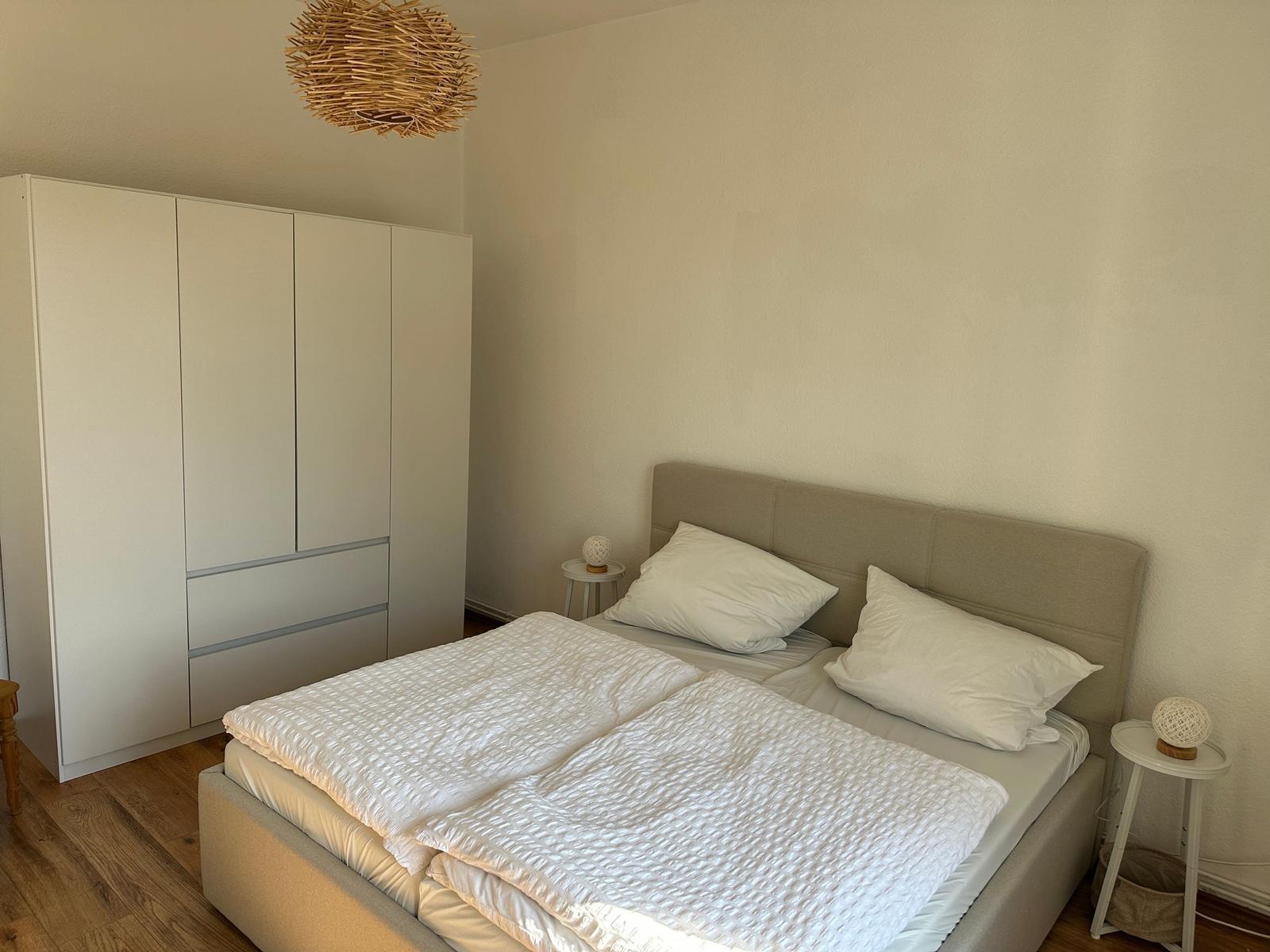 Schlafzimmer mit Doppelbett, weißen Kissen, Nachttischen und Kleiderschrank.