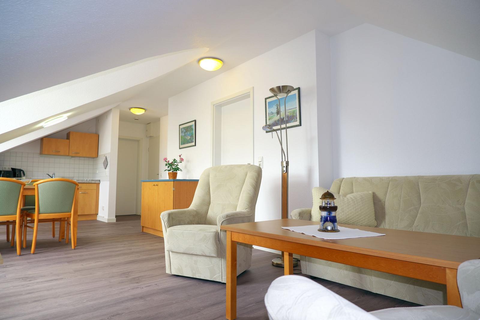 Wohn- und Essbereich mit Sofa, Sessel und Küchenzeile unter Dachschräge.