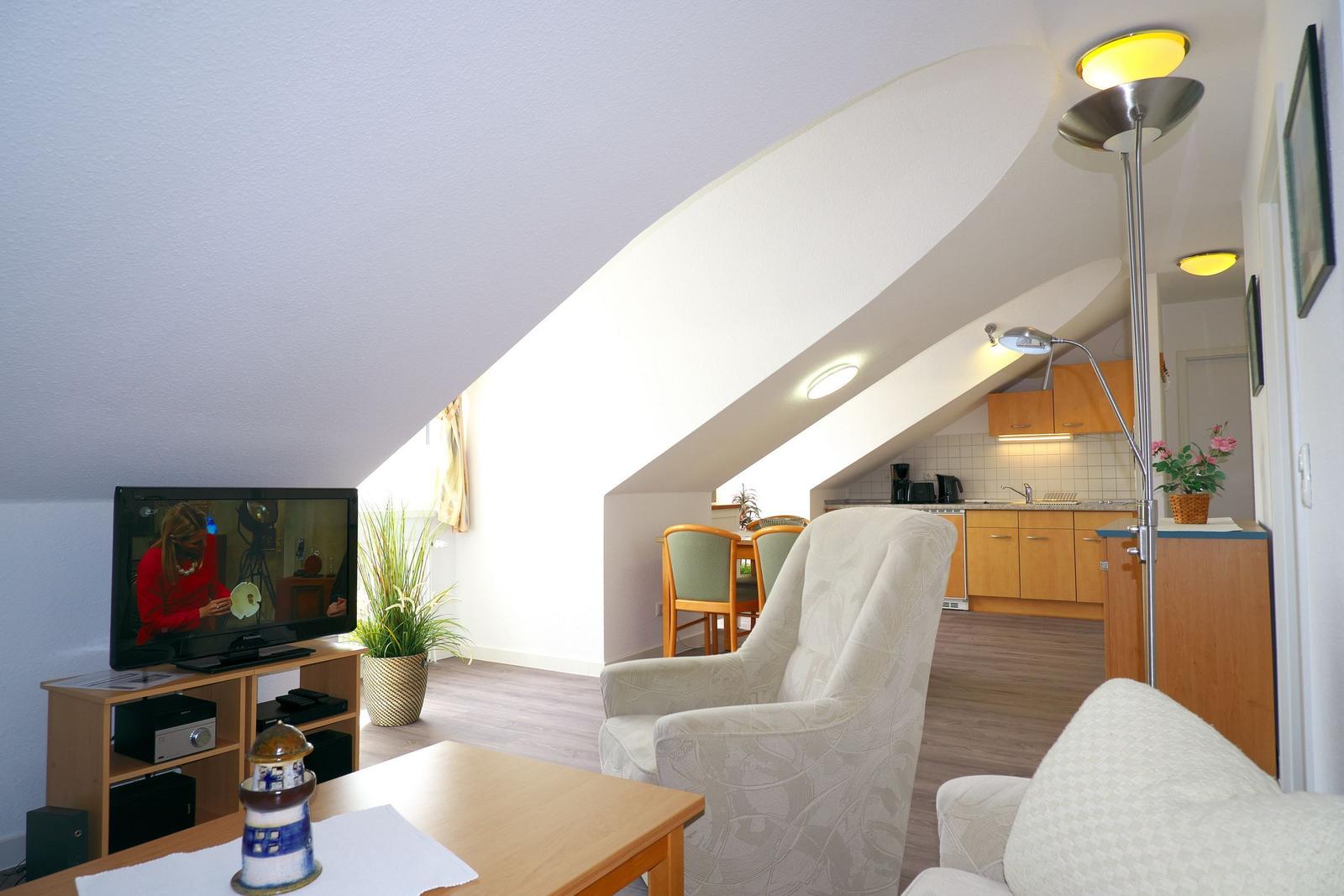 Wohnbereich mit TV, Sessel und Küchenbereich unter Dachschräge.