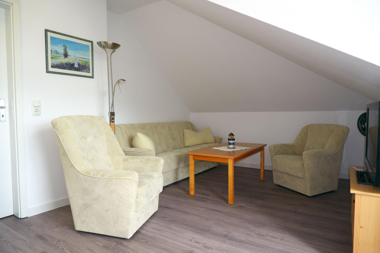 Wohnzimmer mit Sofa, zwei Sesseln und Holztisch unter schrägem Dach