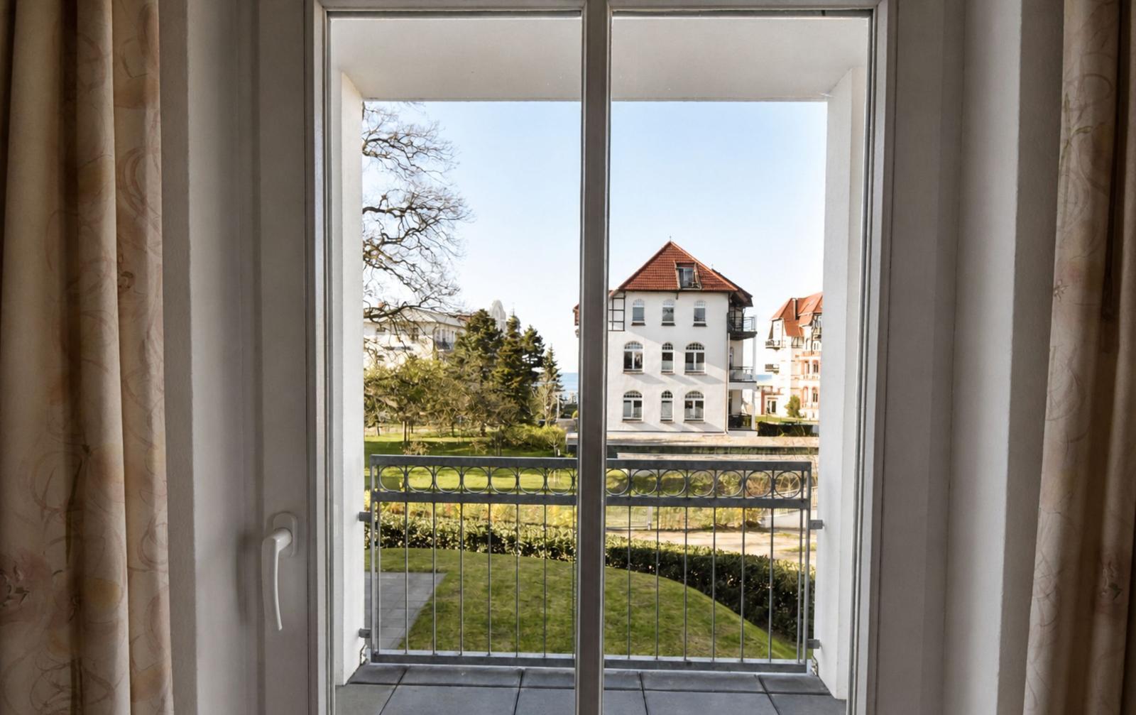 Durch die Glastür blickt man auf eine Terrasse mit Blick auf Grünflächen und Gebäude.