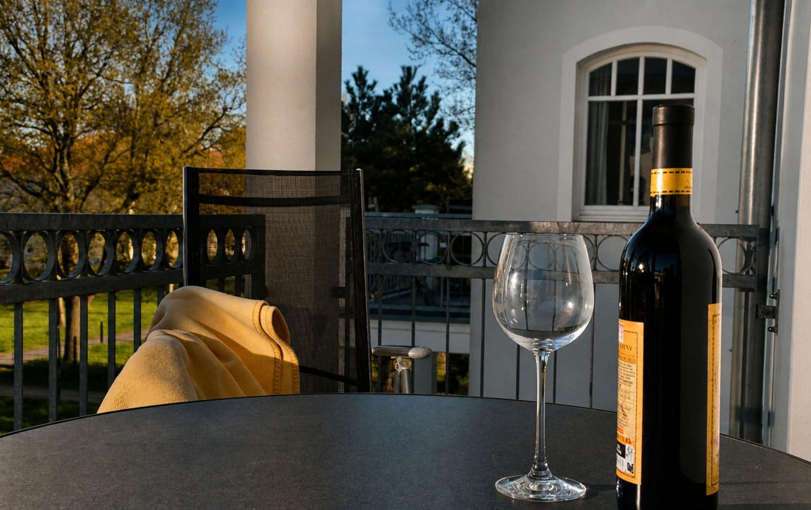 Auf der Terrasse steht ein Tisch mit Weinglas und Flasche. Hintergrund: Haus und Bäume.