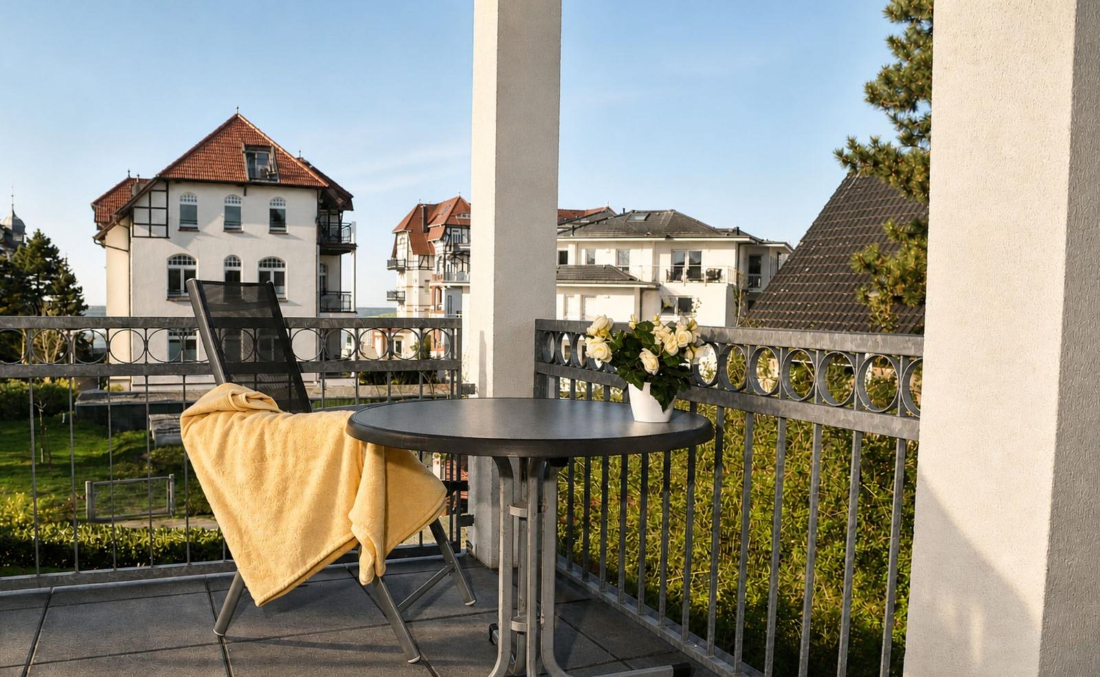 Balkon mit Tisch, Stuhl und Blumen. Blick auf Häuser und Grünflächen.