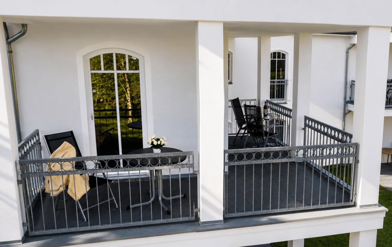 Terrasse mit Tisch, Stühlen und Blumen vor weißer Fassade.