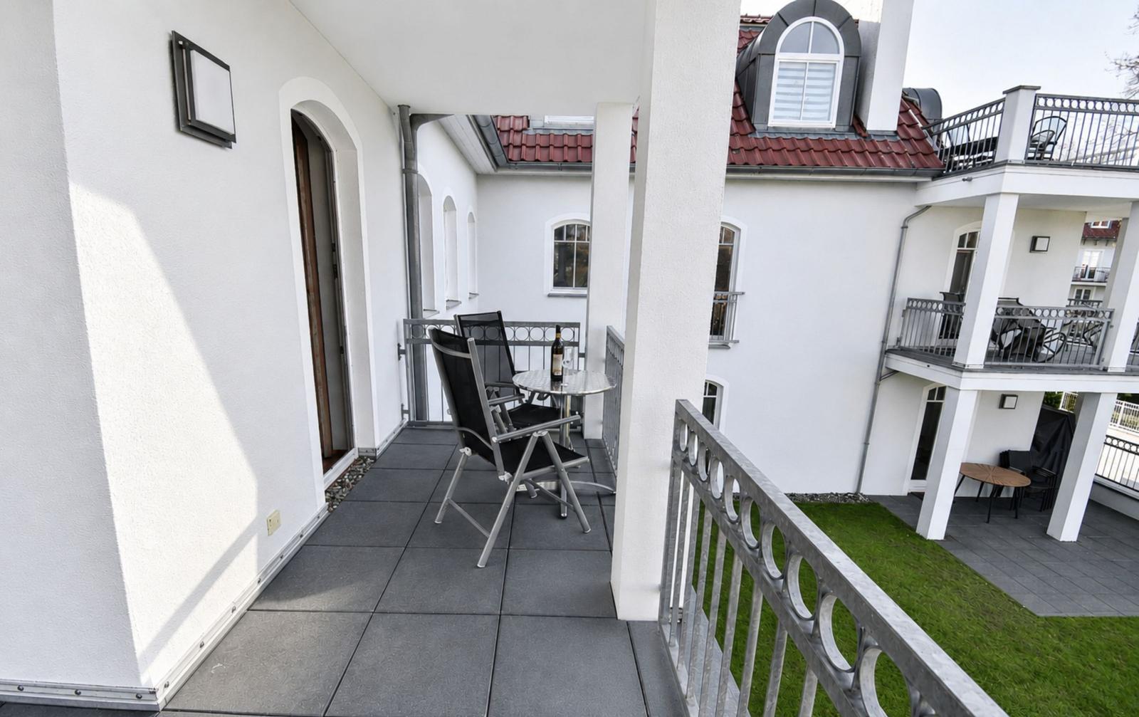 Terrasse mit Tisch und Stühlen, Blick auf Wohnhaus mit Balkon und Dachfenster.
