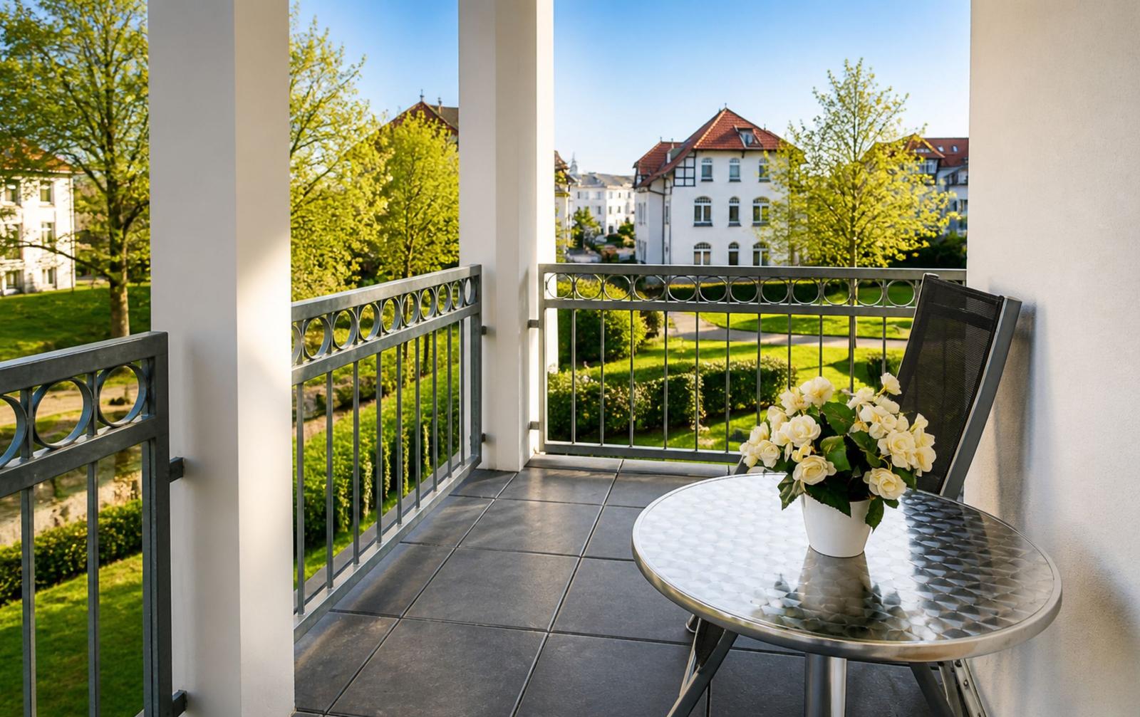Balkon mit Tisch, Stuhl und Blumen. Blick auf Grünfläche und Gebäude.