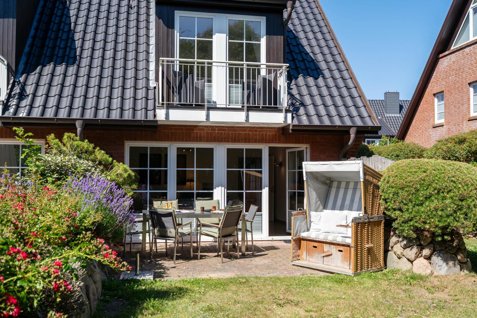 Haus mit Balkon, Terrasse und Garten. Außentisch, Stühle und Strandkorb.