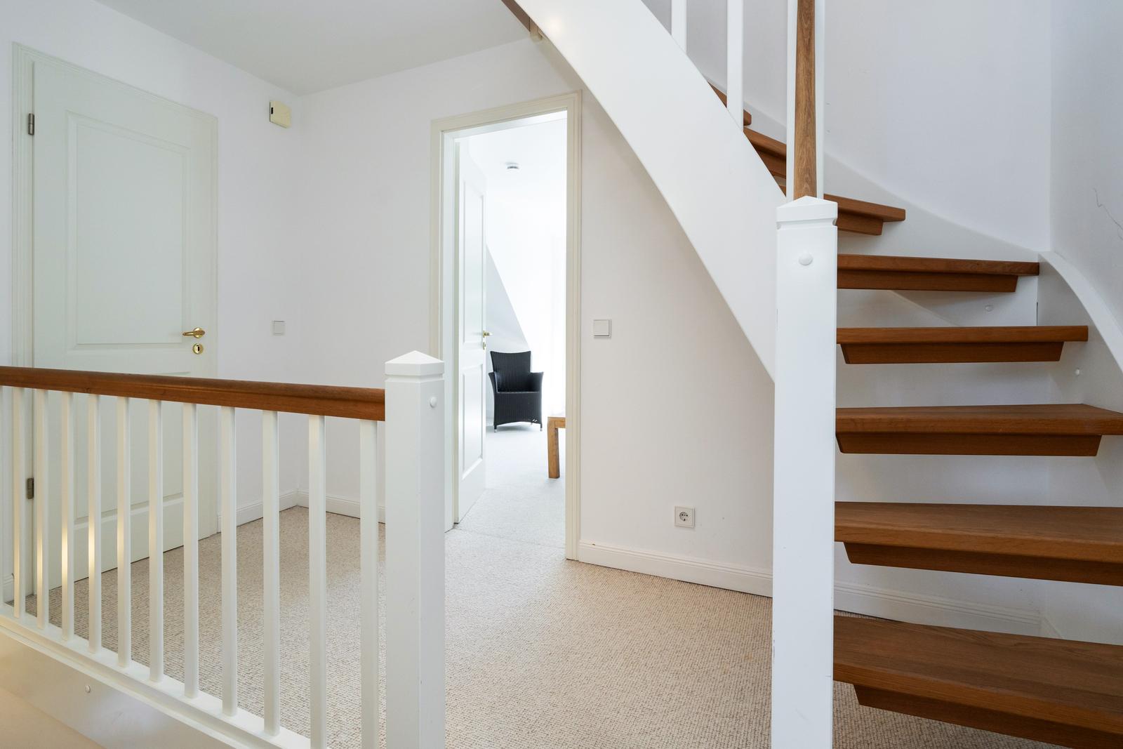 Haus mit Holztreppe und weißen Wänden. Durchgang zu einem Raum mit Stuhl.