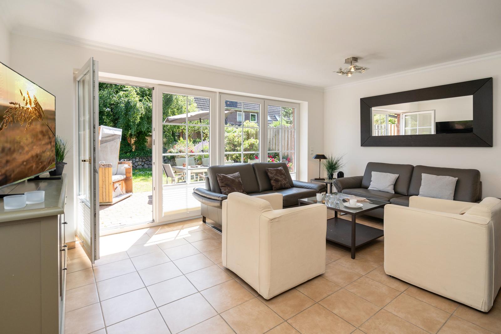 Wohnzimmer mit Sofa, Sesseln und Terrassentür. Fernseher und Spiegel an der Wand.