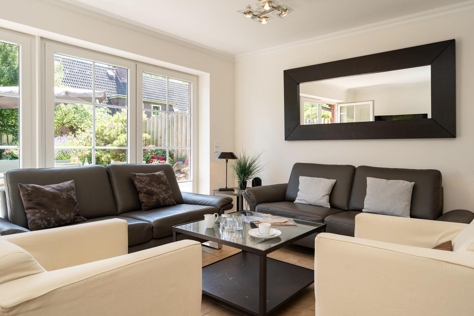 Wohnzimmer mit zwei Sofas, Glas-Tisch und großer Spiegelfläche an der Wand.