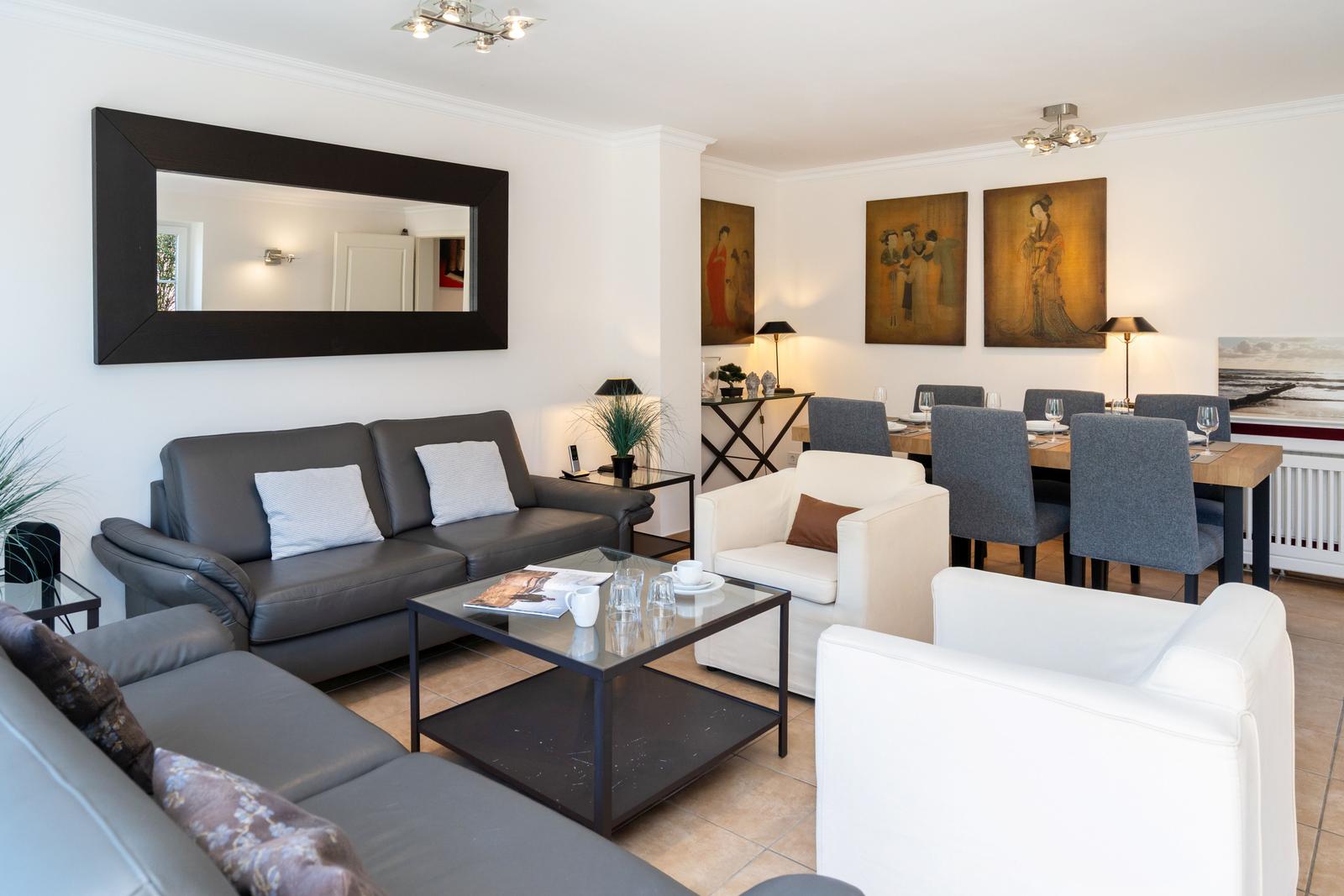 Wohn- und Essbereich mit Sofa, Sesseln und Tisch. Wandbildern und Spiegel.