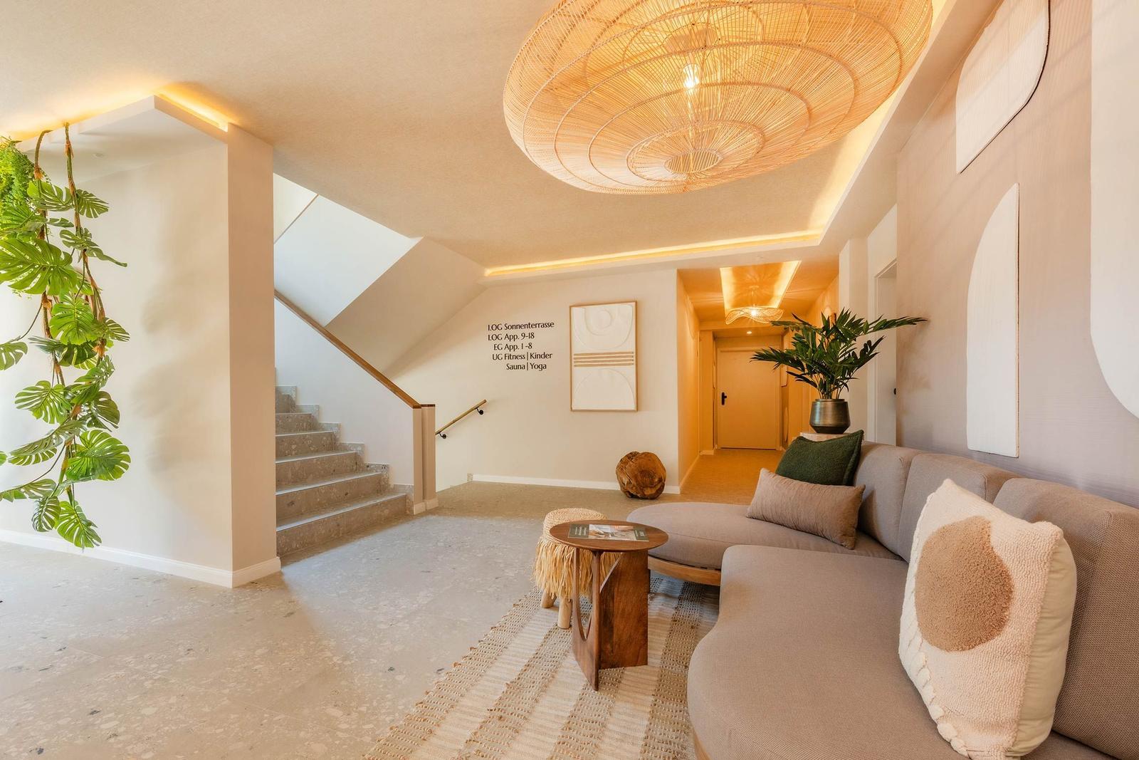Wohnbereich mit Sofa, Tisch und Pflanzen. Treppenhaus und Deckenleuchte sichtbar.