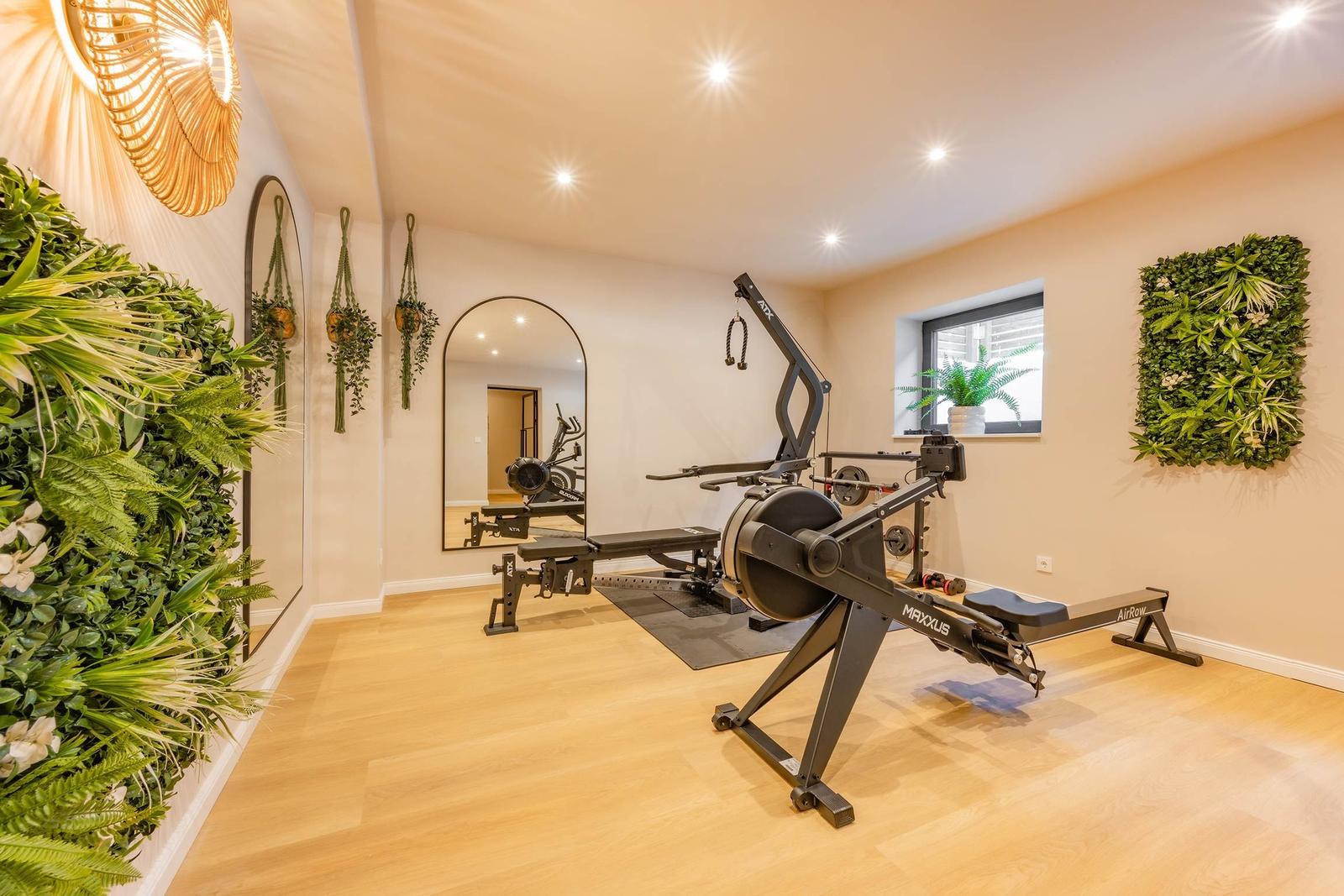 Fitnessraum mit Rudergerät, Spiegeln und Pflanzenwand.