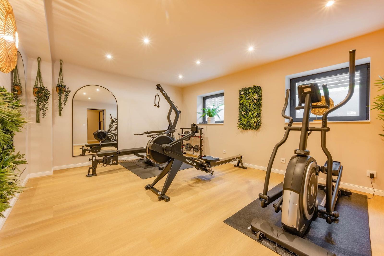 Fitnessraum mit Laufband und Rudergerät, Holzboden und Pflanzen an den Wänden.