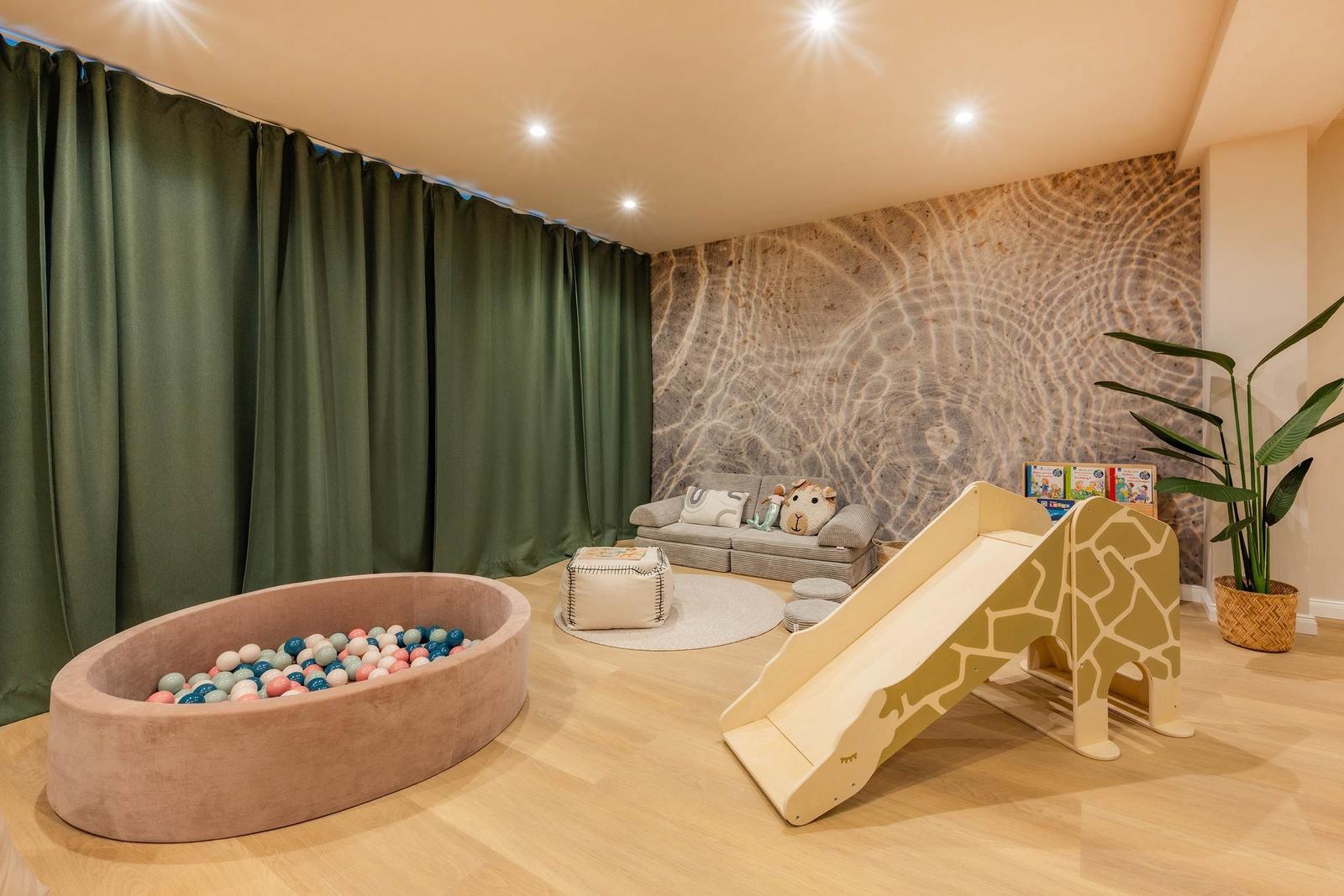 Kinderzimmer mit Ballbad, Giraffenrutsche und Sofa an der Steinwand.