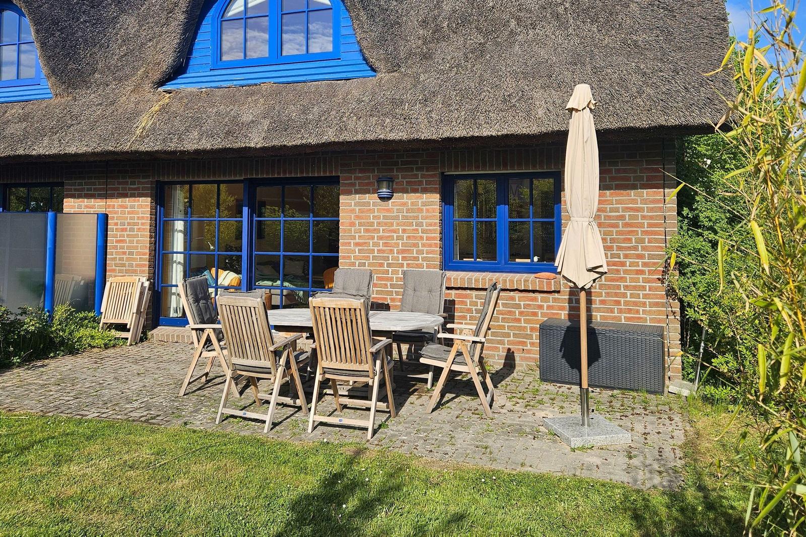 Haus mit Strohdach und Terrasse mit Sitzgruppe und Sonnenschirm.