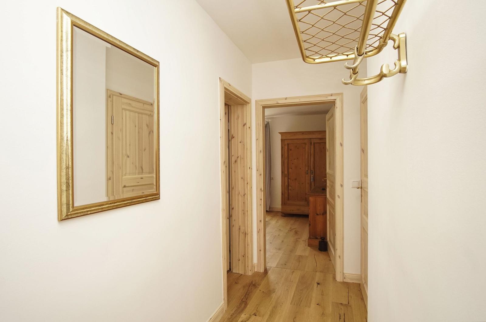 Flur mit goldfarbenem Spiegel und Kleiderständer. Holzfußboden und Türen im Hintergrund.