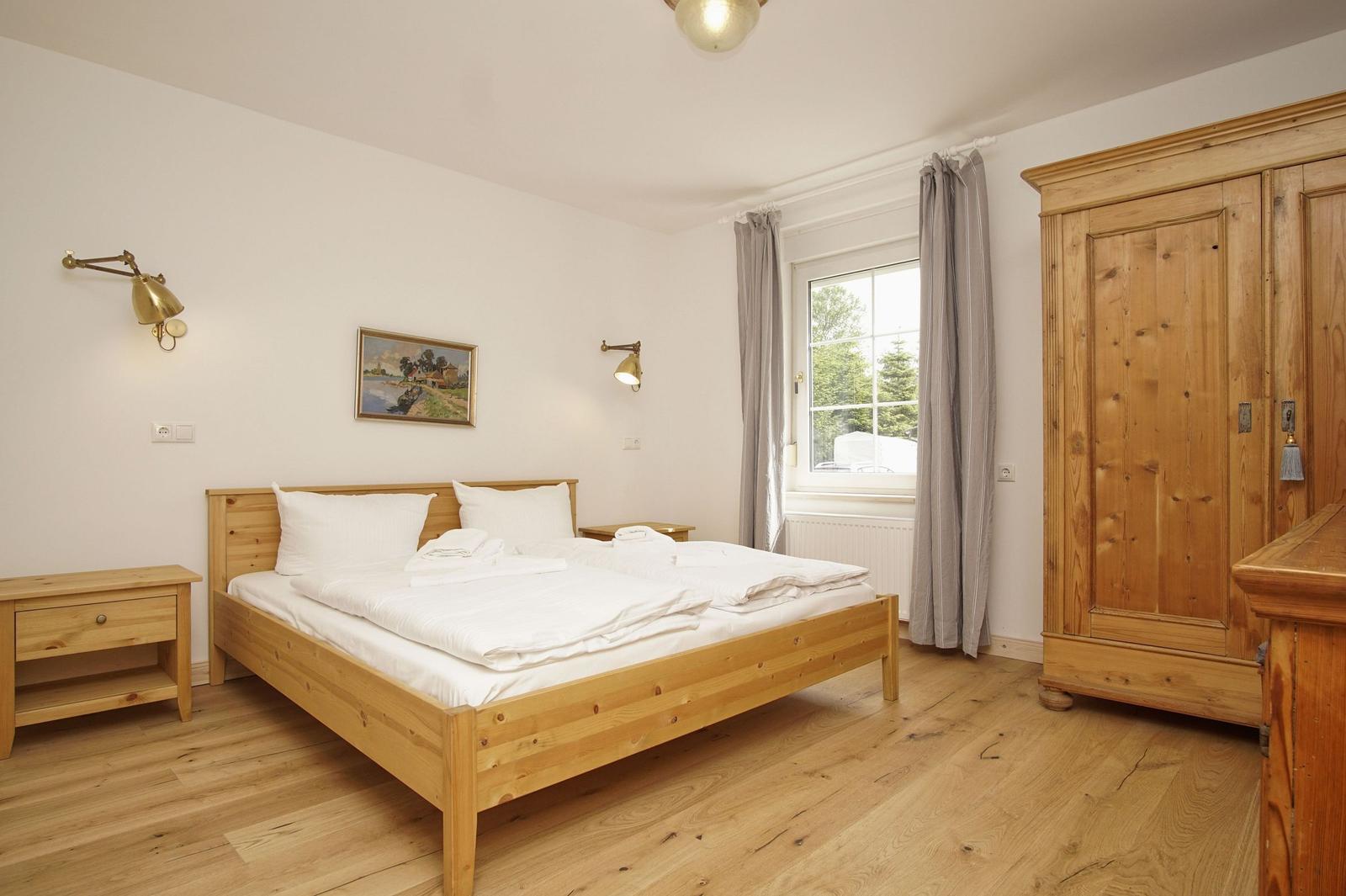 Schlafzimmer mit Holzbett, Kleiderschrank und Fenster mit Blick nach draußen.