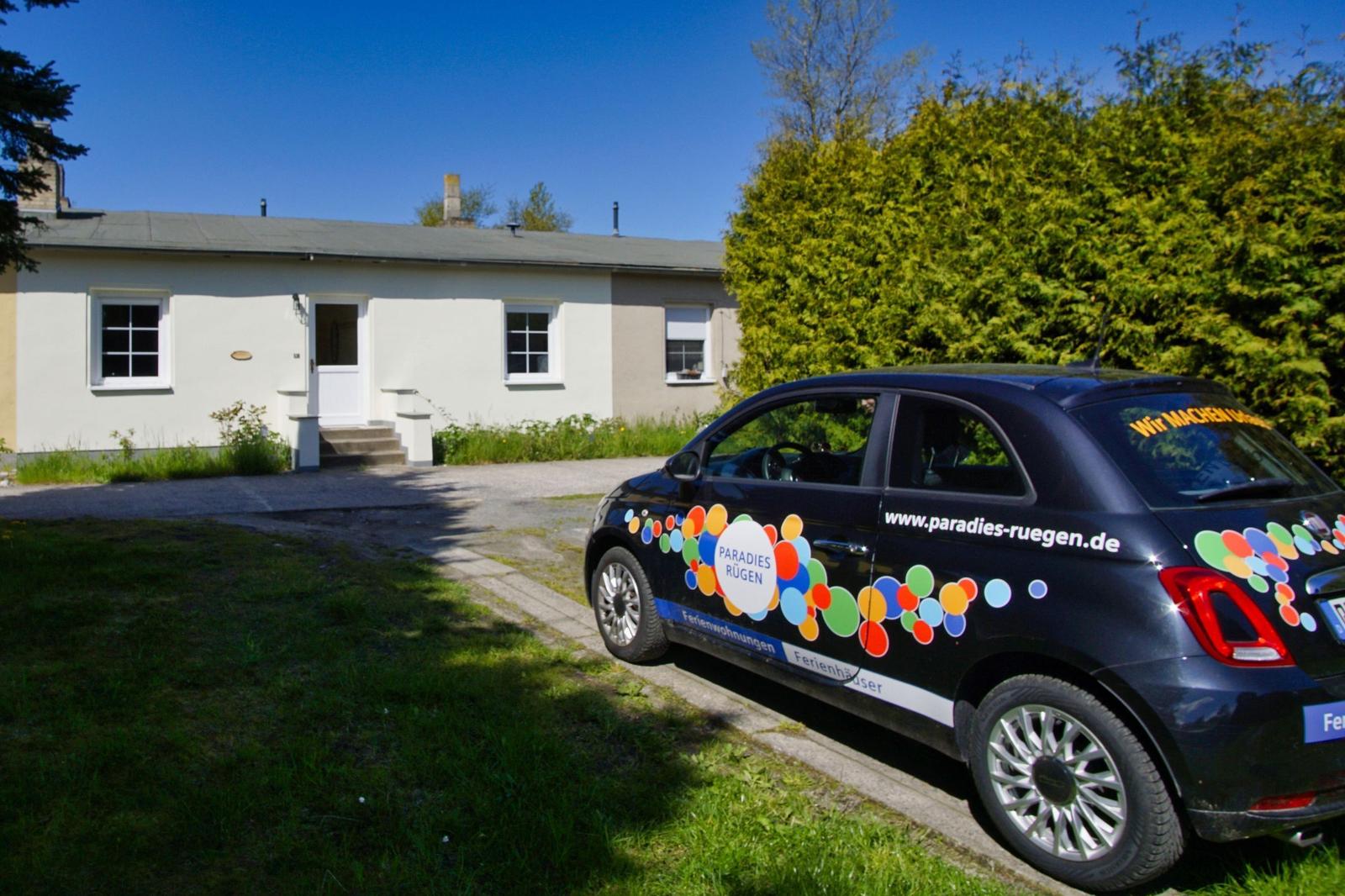 Ein kleines Haus mit einer Garage und einem geparkten Auto vor dem Eingang.