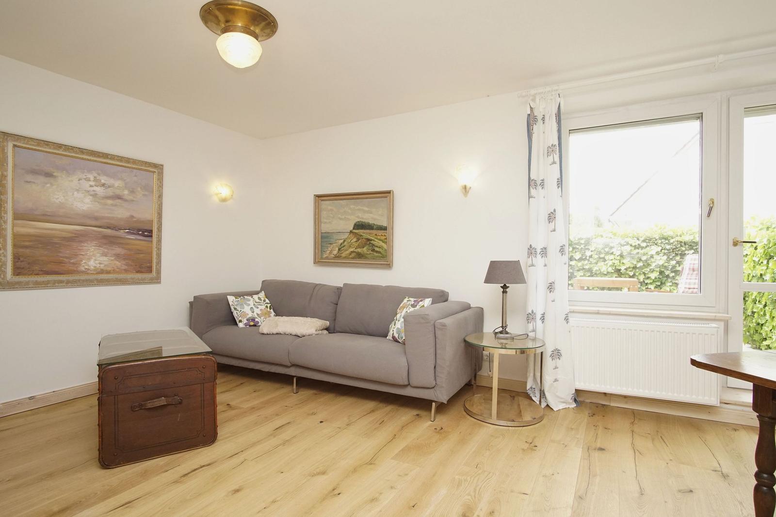 Wohnzimmer mit grauem Sofa, Holzboden und Fenster zur Außenterrasse.
