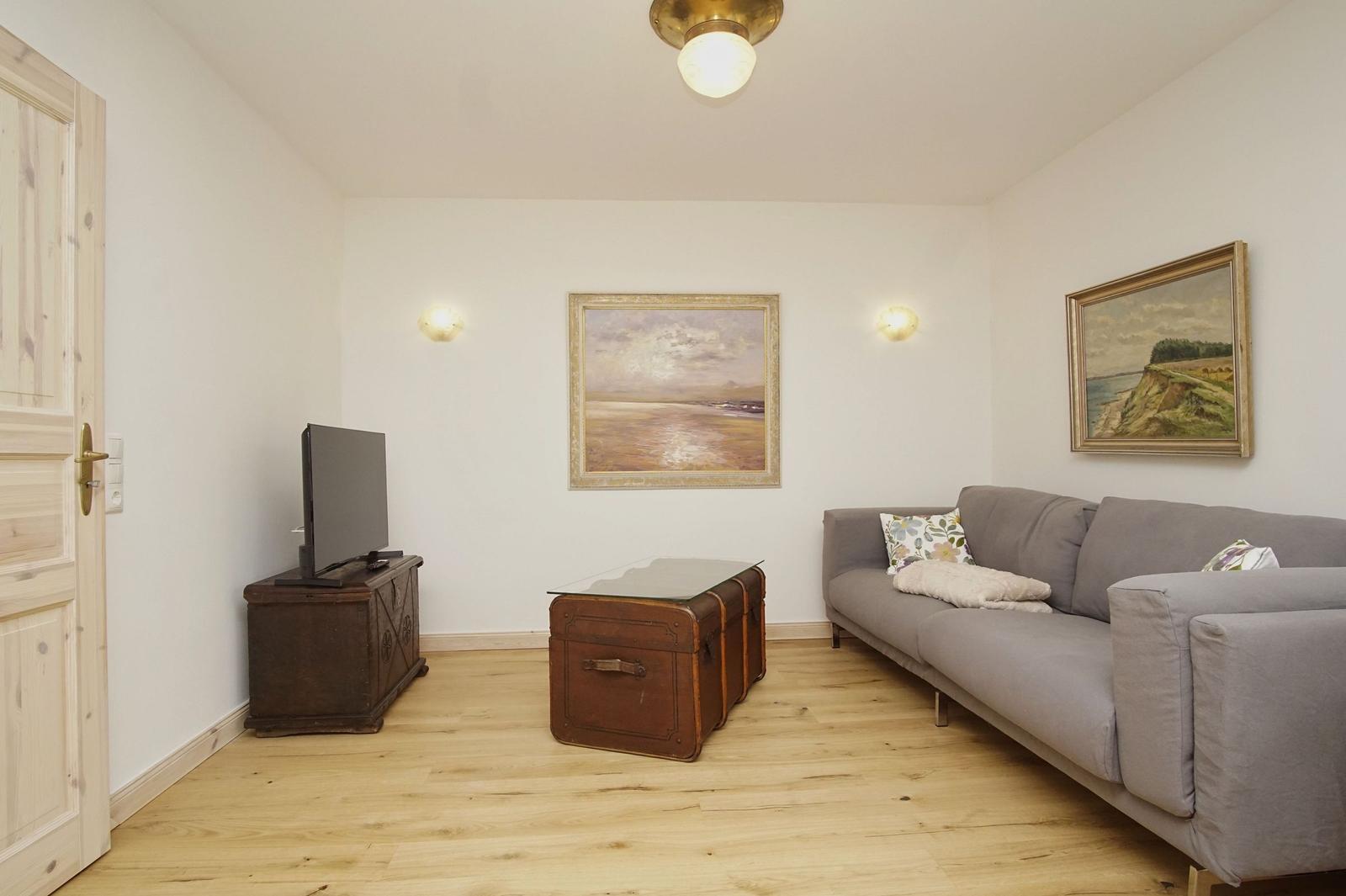 Wohnzimmer mit Sofa, Fernseher und Holzboden. An den Wänden hängen zwei Bilder.