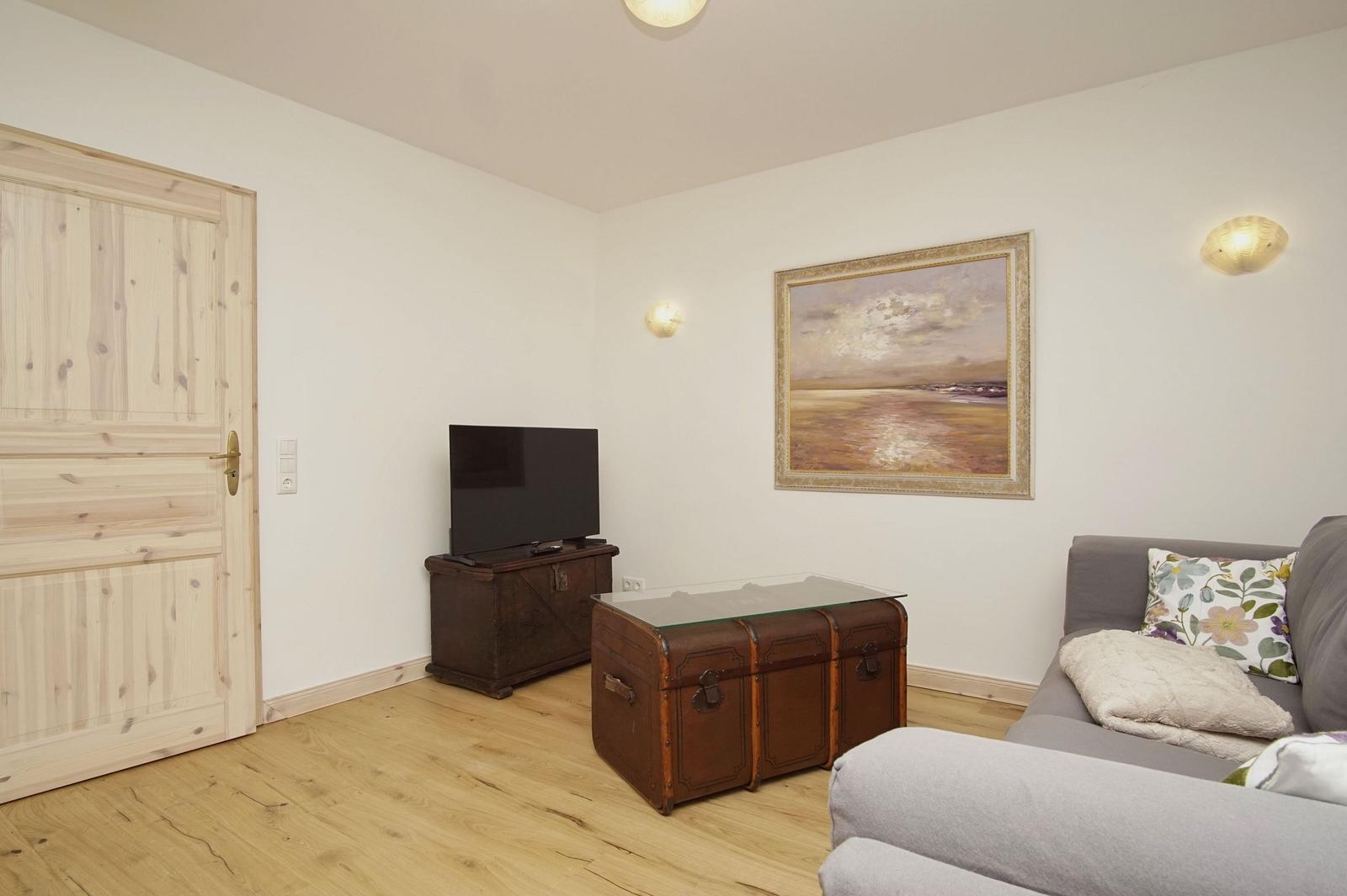 Wohnzimmer mit Sofa, Fernseher und Holzboden. An der Wand hängt ein Bild.