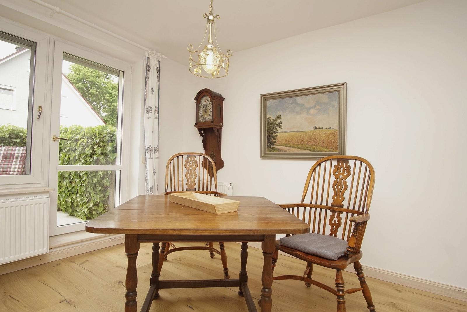 Esszimmer mit Holztisch, zwei Stühlen, Wanduhr und Gemälde an der Wand.