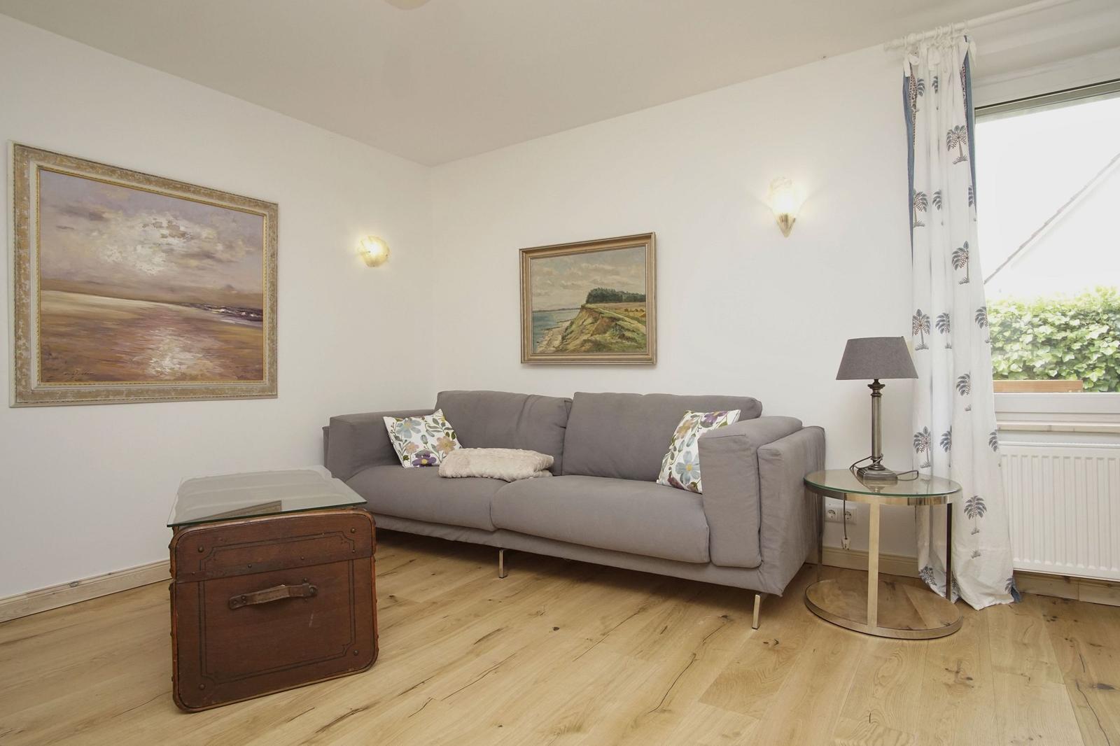 Ein Wohnzimmer mit grauem Sofa, Holzboden und zwei Wandbildern an der Wand.