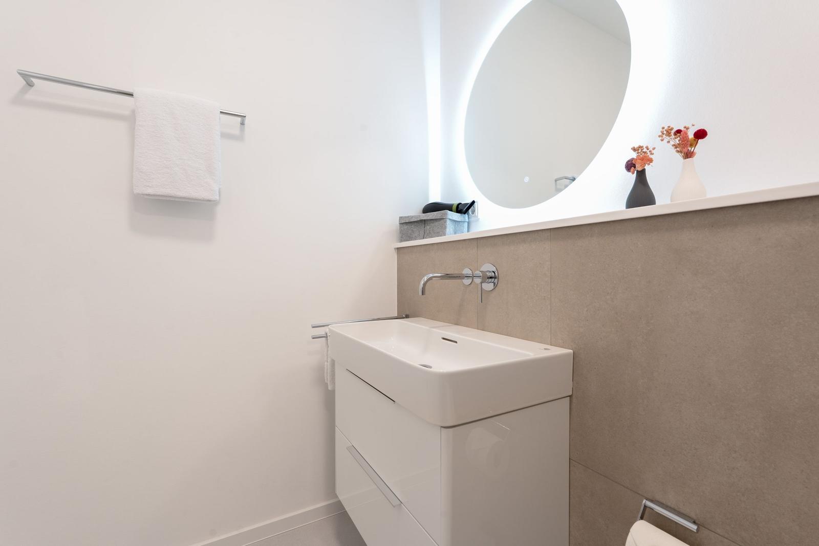 Badezimmer mit Waschbecken, Spiegel und Handtuchhalter.